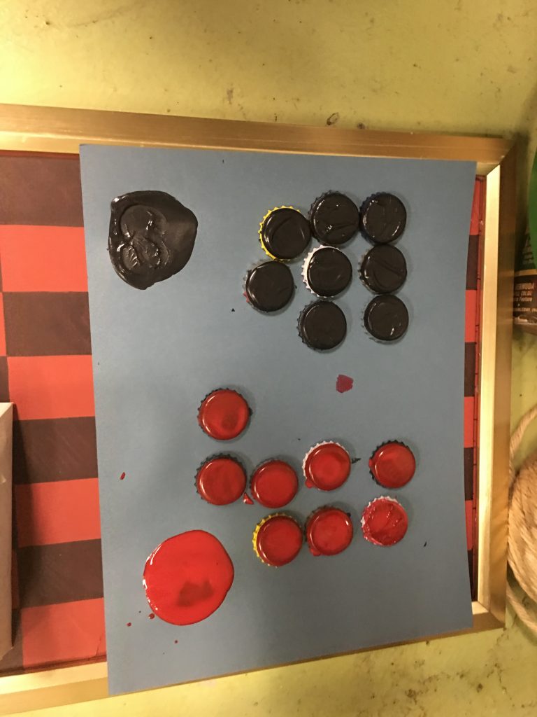 homemade checkerboard with round black pieces and red pieces