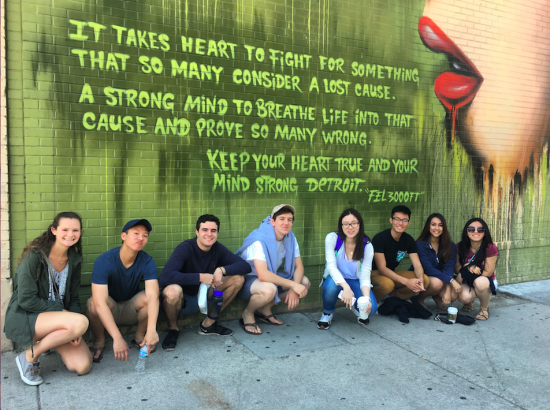 students squat in front of mural that reads "It takes heart to fight for something that so many consider a lost cause. A strong mind to breathe life into that cause and prove so many wrong. Keep your heart true and your mind strong Detroit. 'Fel 3000ft'"