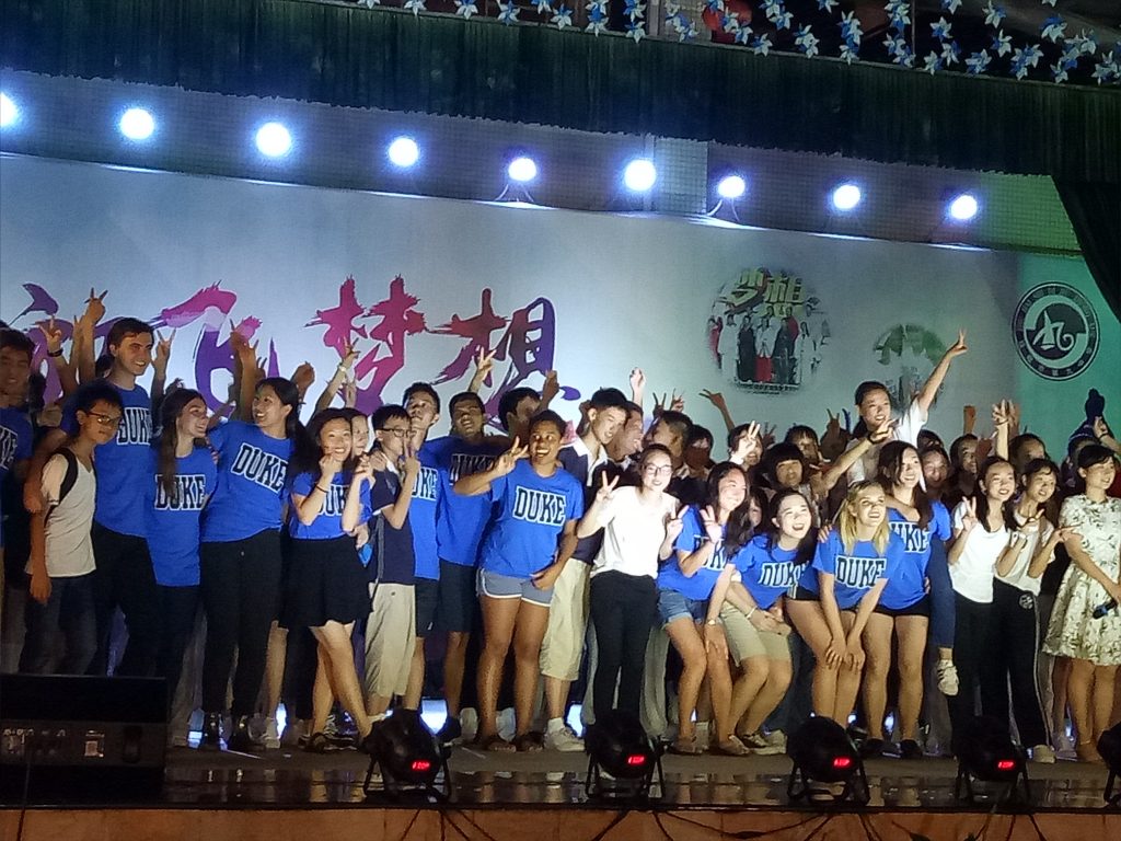 large group of performers dancing on stage wearing duke tshirts