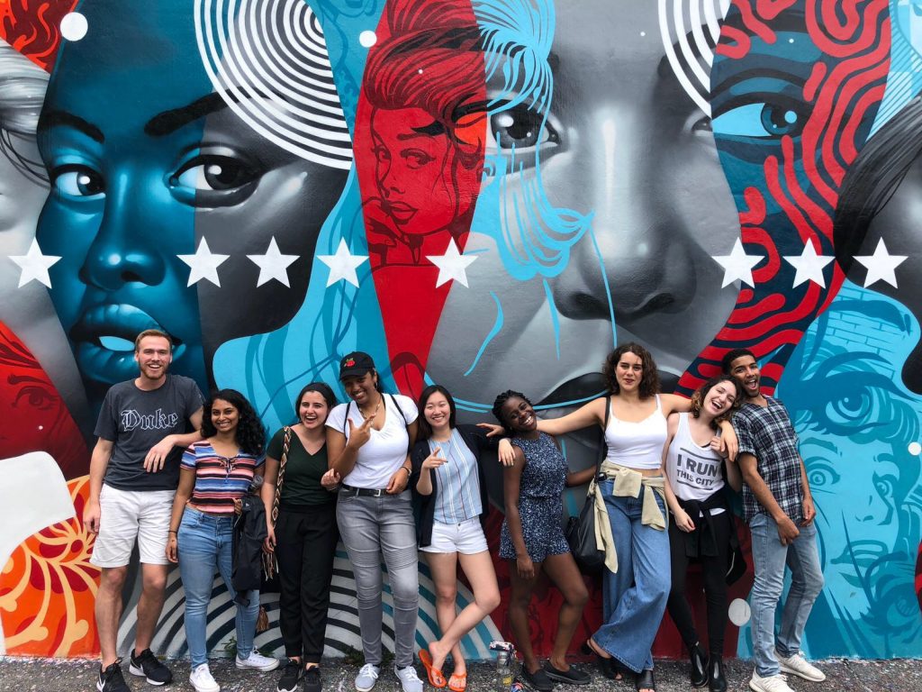 group of young people posing for photo in front of a large, colorful mural