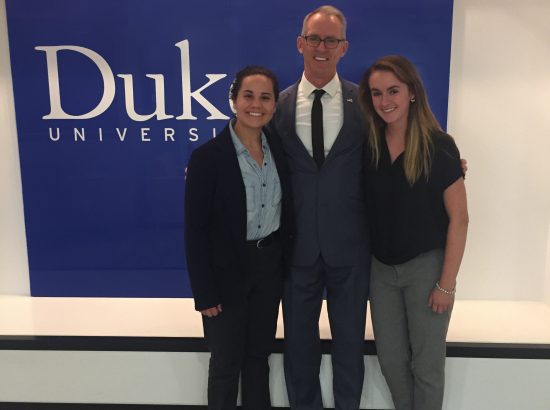 three poeple posing for camera in front of large blue banner with the word Duke on it