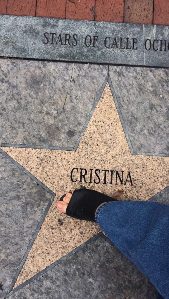 womans foot in a black sandal steps on a star in the sidewalk with the name Cristina printed in it