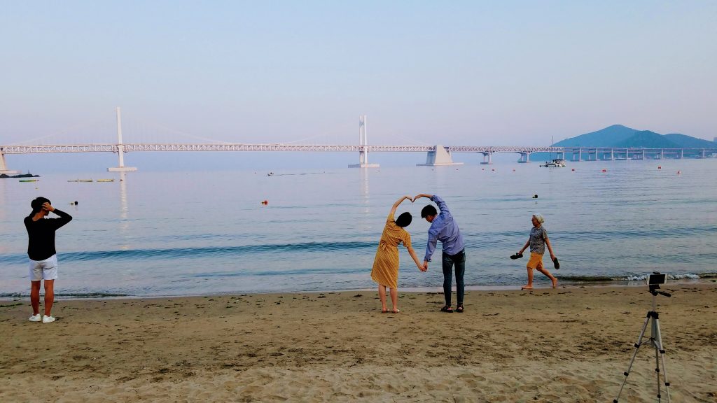 view of a beach and a bridge with a couple making a heart with their arms