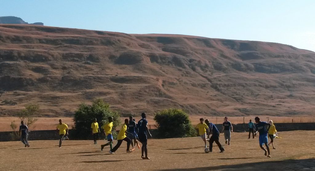 people playing soccer in a field in front of the Drakensberg mountains