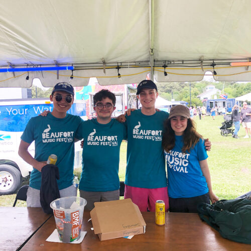 Students pose under a tent, wearing blue t-shirts reading "Beaufort Music Festival."