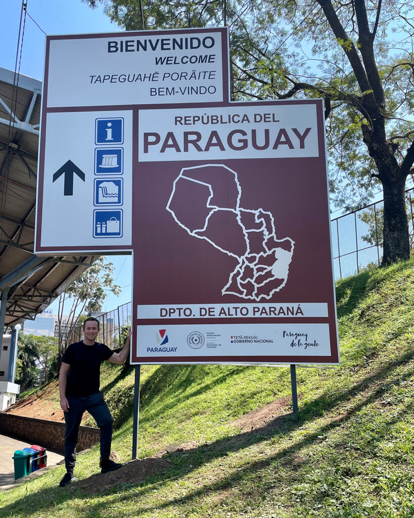 Austin Connors in front of a sign welcoming people to Paraguay