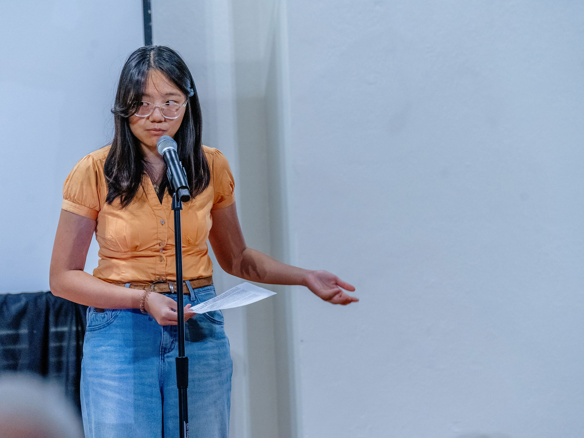 A young woman gestures as she speaks at a microphone