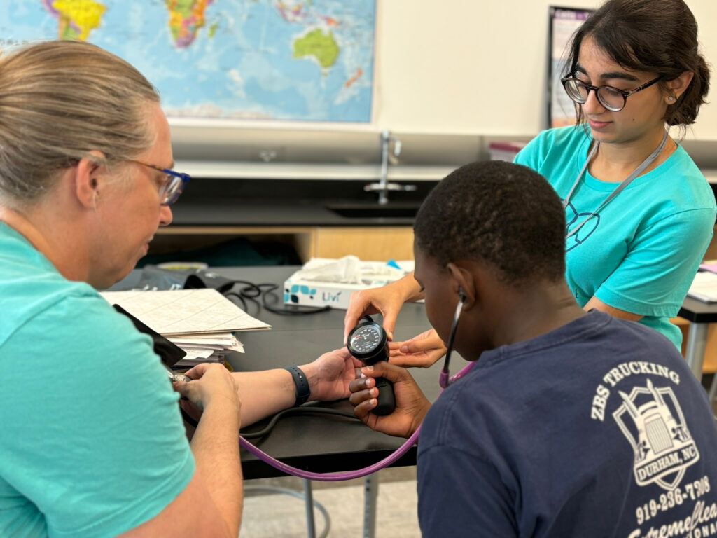 A young woman assists a young man in taking a woman's blood pressure 